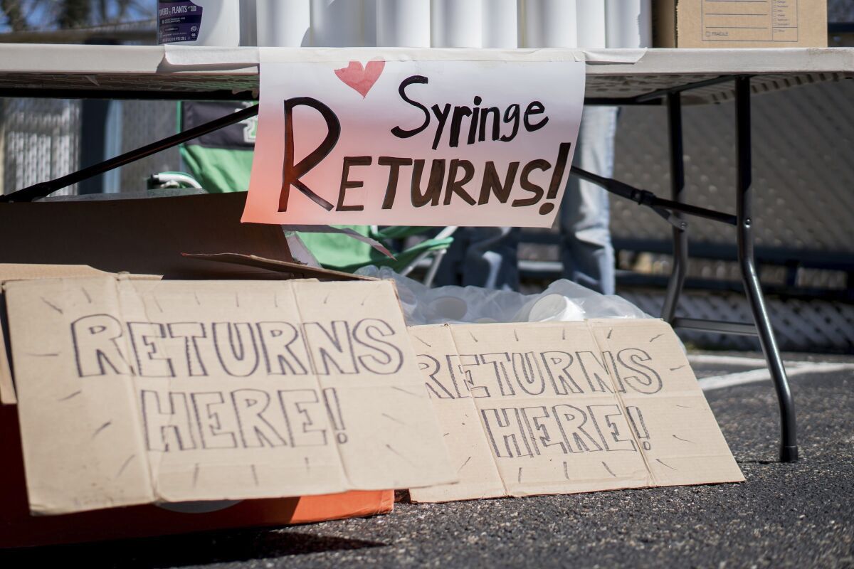 In this photo provided by Chad Cordell, signs for syringe returns are shown Saturday, March 6, 2021, at a nonprofit group's health fair in Charleston, W.Va. For years, West Virginia has had the nation's highest rate of drug overdose deaths. Now the state is wrestling with another, not entirely unrelated health emergency: a spike in HIV cases related to intravenous drug use. (Chad Cordell via AP)