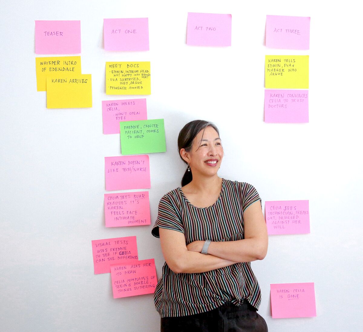 A smiling woman stands in front of a wall featuring colorful cards with writing on them.