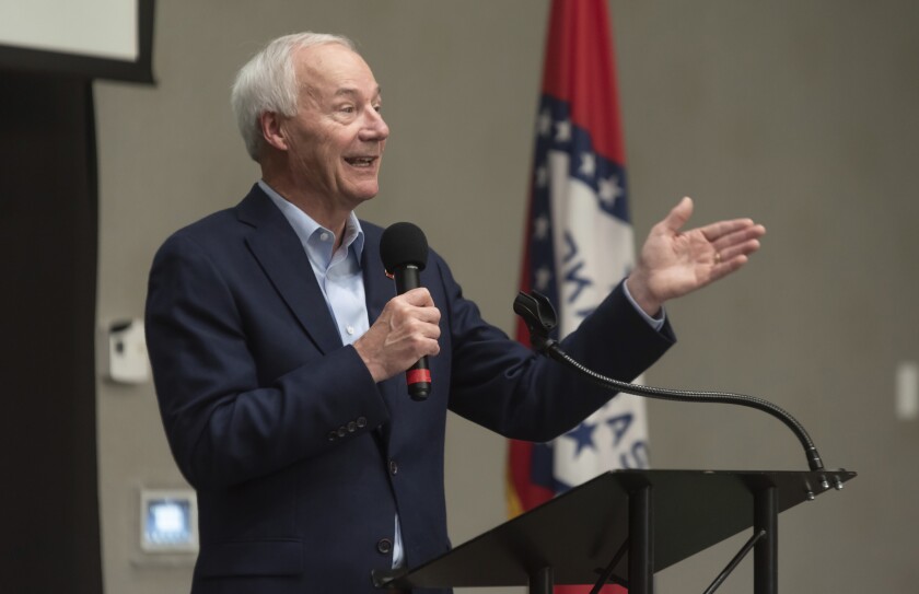 Arkansas Gov. Asa Hutchinson holds a microphone as he speaks behind a lectern. 