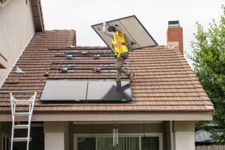 A solar panel installer carries a panel as he walks on the top of a roof.