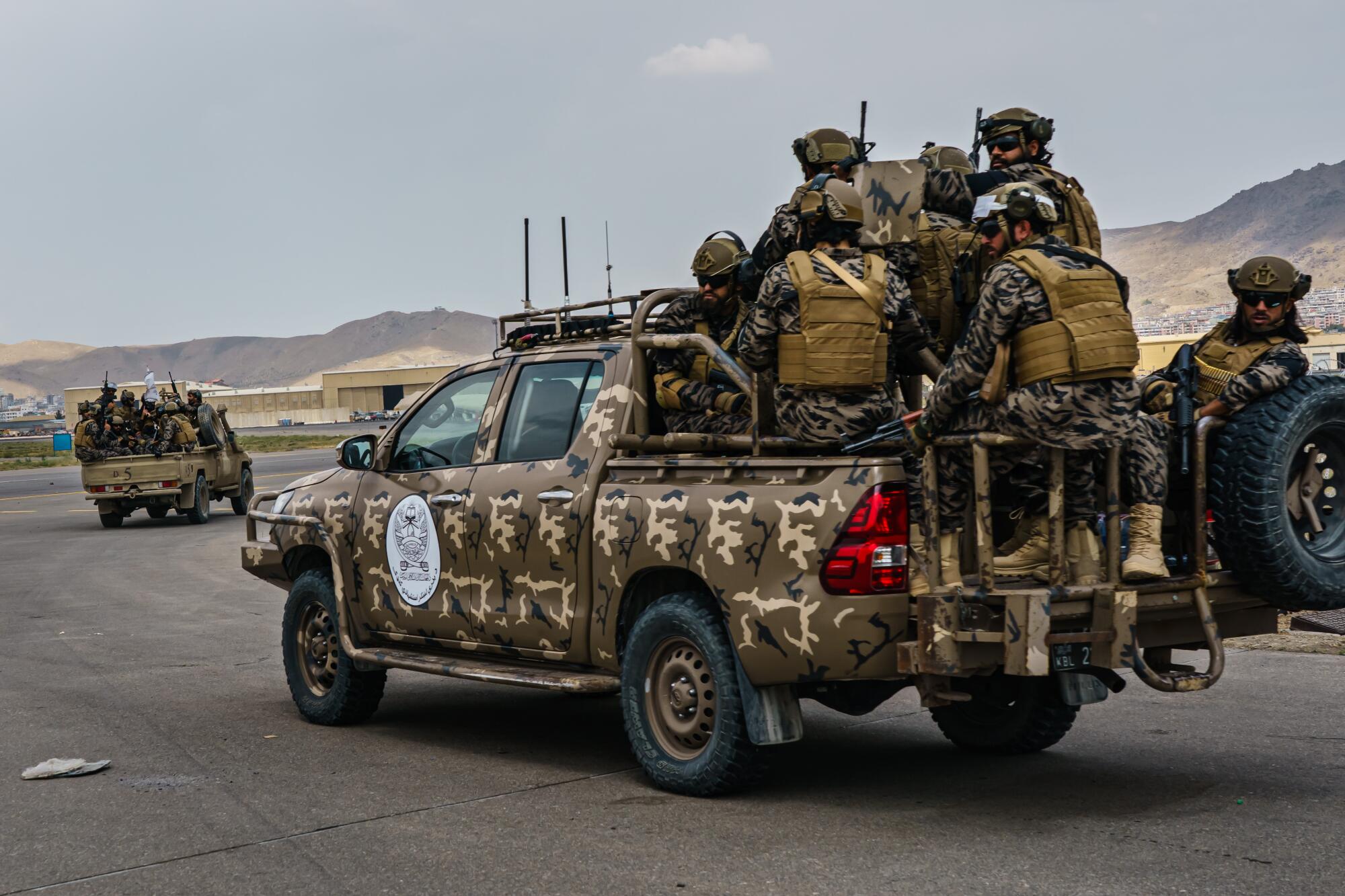 Taliban fighters ride in camouflage pickup trucks