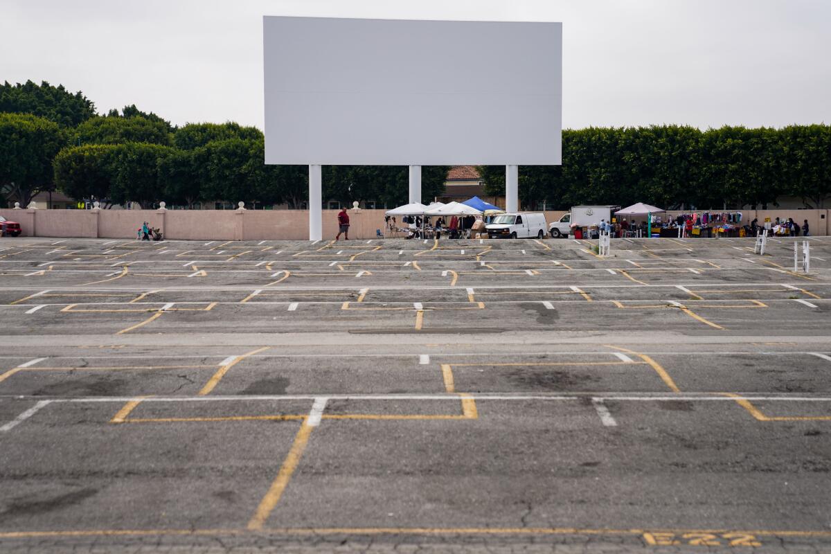 A few cars and vendor booths sit under the drive-in movie screen on a mostly empty parking lot at the Paramount Swap Meet