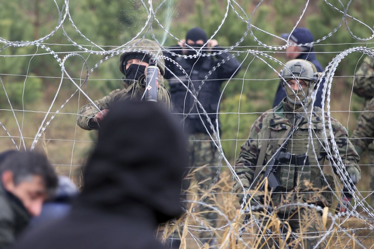 Polish border guards stand near the barbed wire as migrants from the Middle East and elsewhere gather at the Belarus-Poland border near Grodno, Belarus, Monday, Nov. 8, 2021. Poland increased security at its border with Belarus, on the European Union's eastern border, after a large group of migrants in Belarus appeared to be congregating at a crossing point, officials said Monday. The development appeared to signal an escalation of a crisis that has being going on for months in which the autocratic regime of Belarus has encouraged migrants from the Middle East and elsewhere to illegally enter the European Union, at first through Lithuania and Latvia and now primarily through Poland. (Leonid Shcheglov/BelTA via AP)