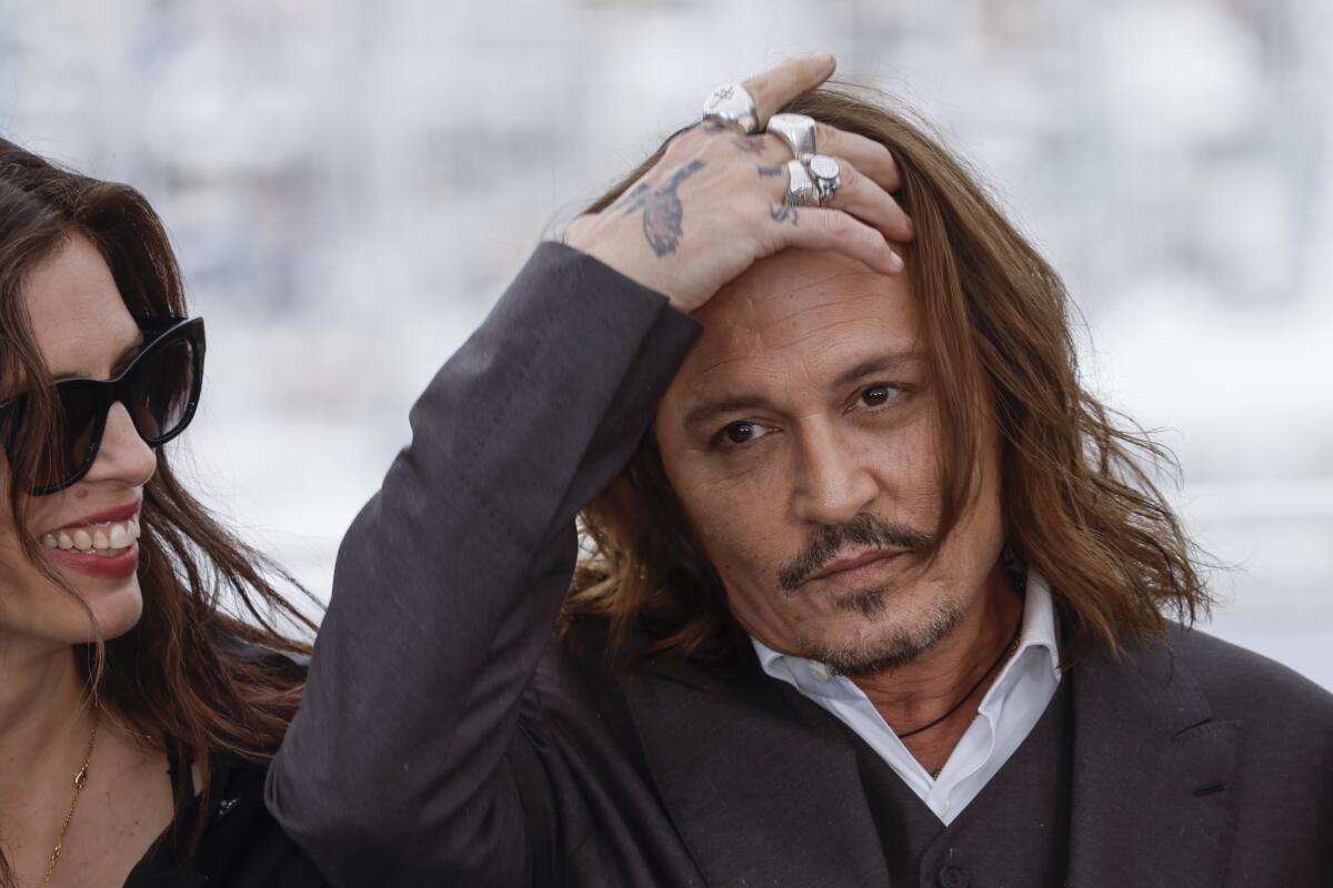 Johnny Depp pushes his hair back as a woman smiles next to him.