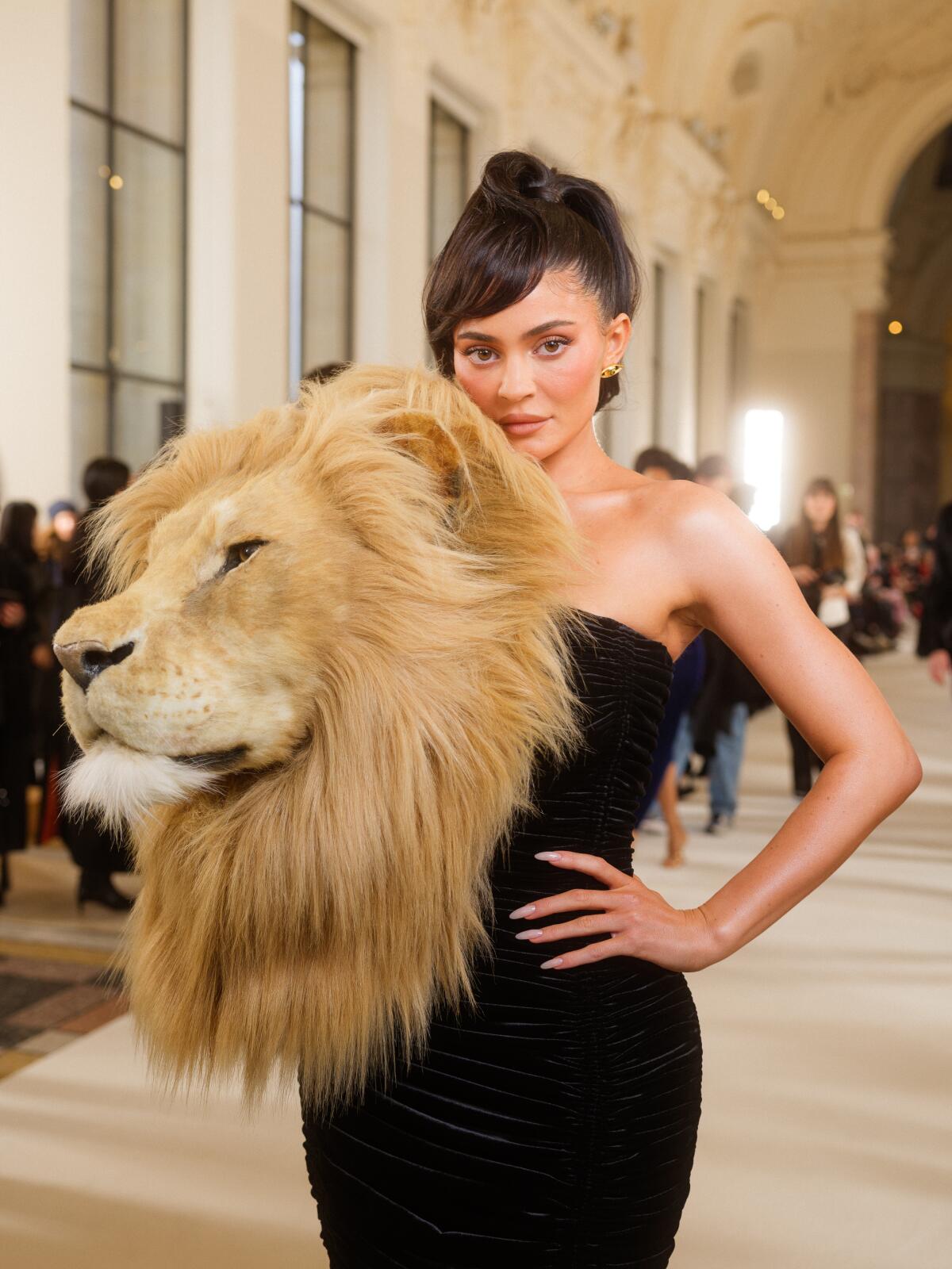 A woman in a form fitting black dress with a lion head on her right shoulder.
