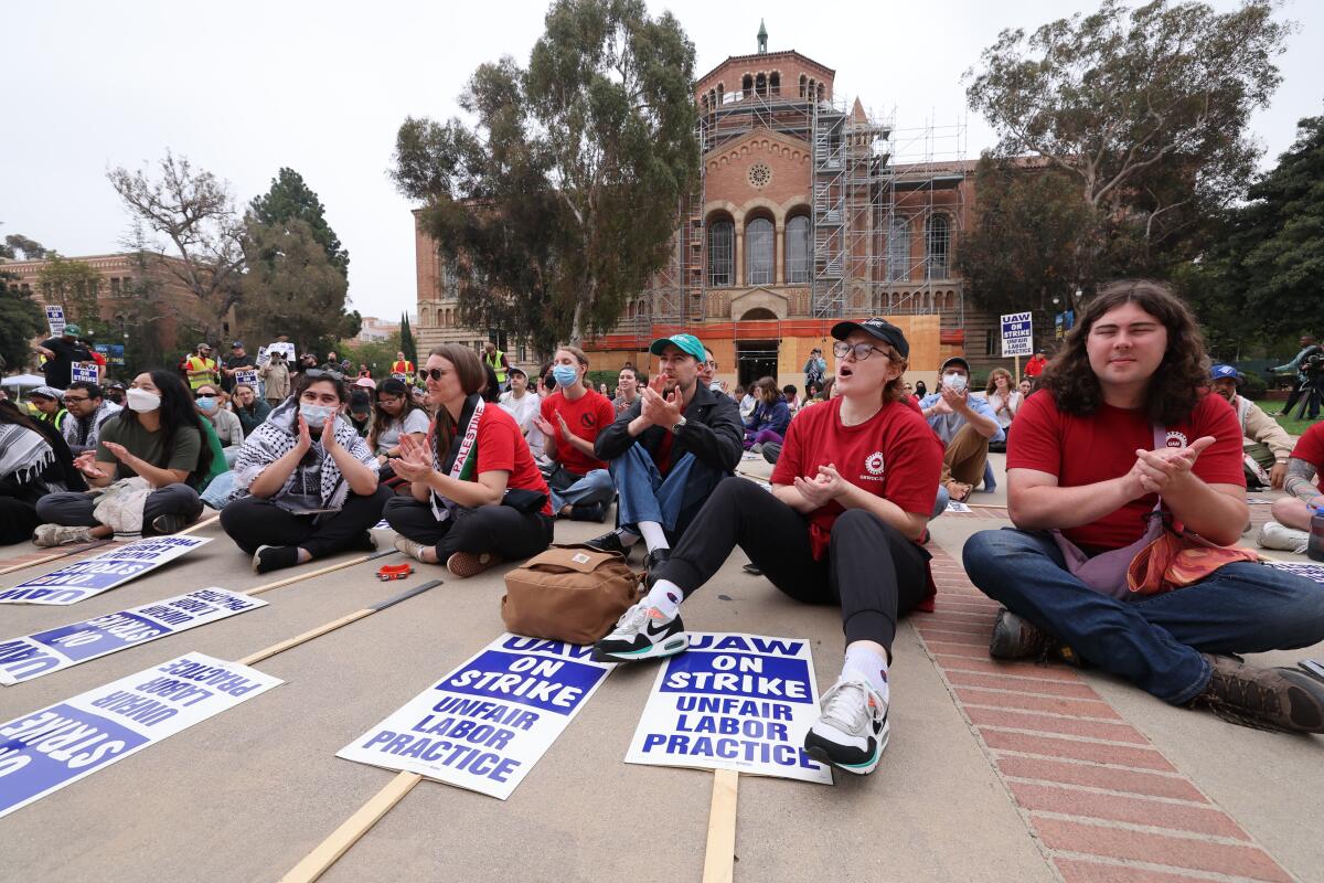 Striking workers sit on the ground with signs at UCLA.