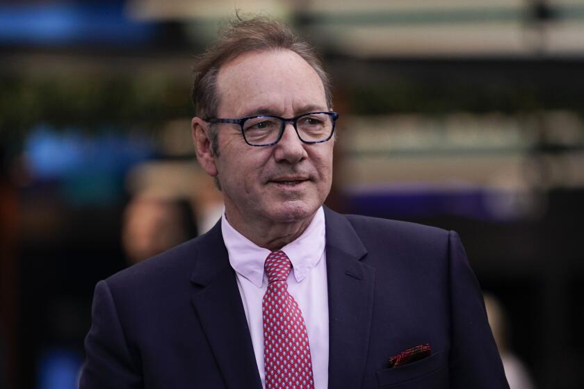 Kevin Spacey wearing glasses, a blue suit, a pink shirt and a red, polka-dot tie.