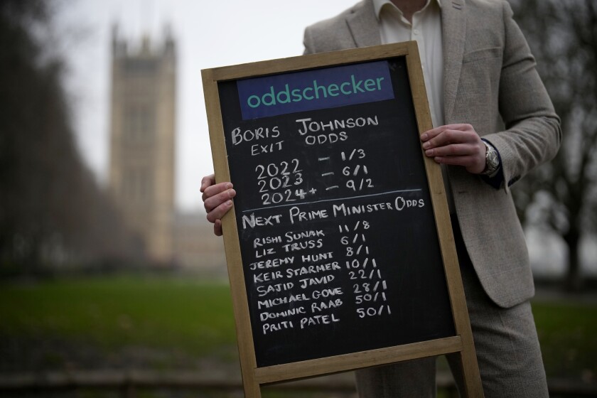 Callum Wilson, senior PR manager at the Oddschecker betting odds comparison company poses for photographs with a betting chalk board showing their odds for British Prime Minister Boris Johnson exiting his role as Prime Minister and odds for who the next Prime Minister might be, backdropped by the Houses of Parliament in London, Friday, Jan. 21, 2022. Some Conservative lawmakers in Britain are talking about ousting their leader, Prime Minister Boris Johnson, over allegations that he and his staff held lockdown-breaching parties during the coronavirus pandemic. The party has a complex process for changing leaders that starts by lawmakers writing letters to demand a no-confidence vote. (AP Photo/Matt Dunham)
