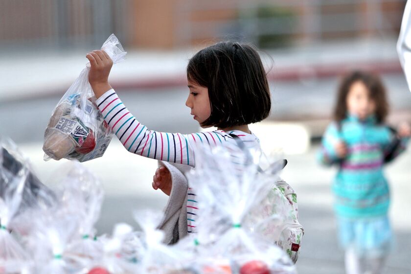 Chelsea Simmons, 7 and a first grader, grabs her breakfast and lunch bag at the Glendale High School parking lot distribution area during the Glendale Unified "Grab and Go Drive Up Service," in Glendale on Tuesday, March 24, 2020. Students get a bag with breakfast and lunch each day.