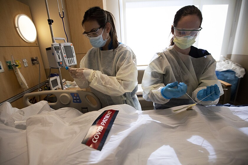 دو پرستار در یک بیمارستان کیسه ای سفید با برچسب را می بندند "بیمار مبتلا به COVID"