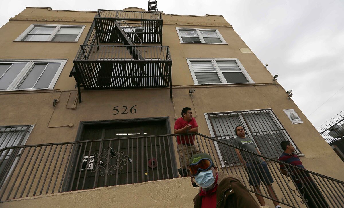 Men stand outside an apartment building in the Westlake District of Los Angeles, which has the second-highest population density in the city, with about 38,214 people per square mile. 