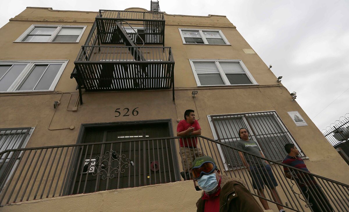 Men stand outside an apartment building in the Westlake District of Los Angeles, which has the second-highest population density in the city, with about 38,214 people per square mile.