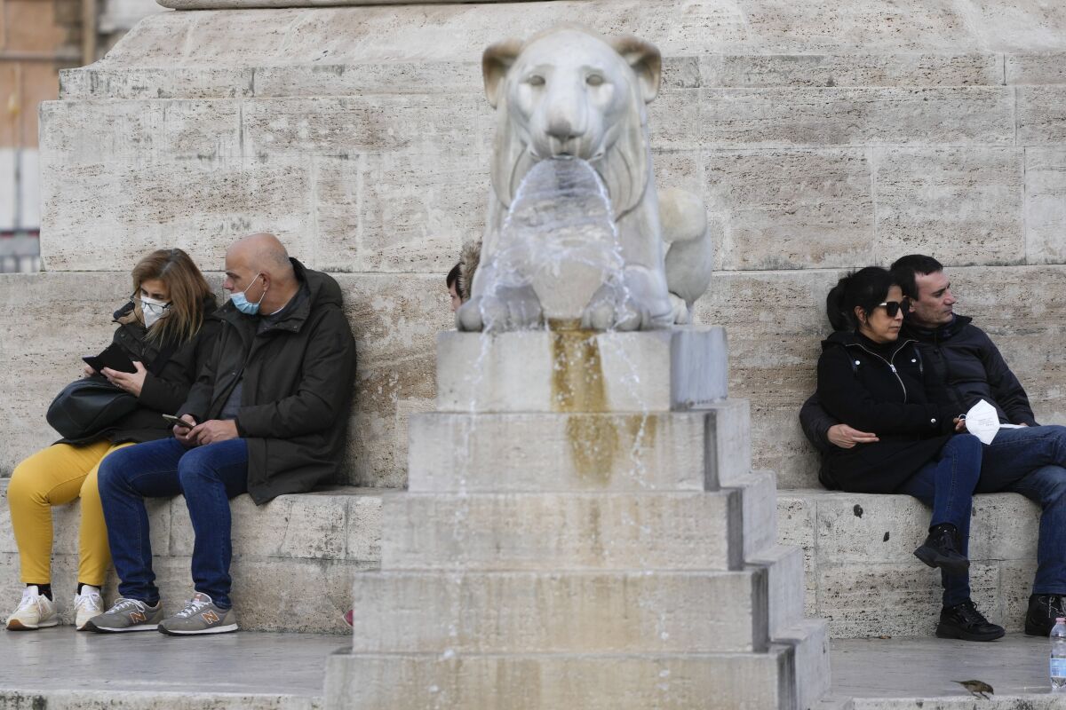 People sit by the Rome's Piazza del Popolo Lions foutain, Wednesday, Jan. 5, 2022. The Italian Government is expected to hold a cabinet meeting with scientific and medical experts Wednesday, to apply new measures to cope with the surge of new COVID-19 cases in the country. (AP Photo/Gregorio Borgia)