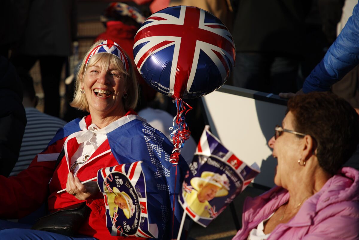 Royal fans share a laugh as they gather along The Mall leading to Buckingham Palace in London, Thursday June 2, 2022, on the first of four days of celebrations to mark the Platinum Jubilee. The events over a long holiday weekend in the U.K. are meant to celebrate the monarch's 70 years of service. (AP Photo/David Cliff)