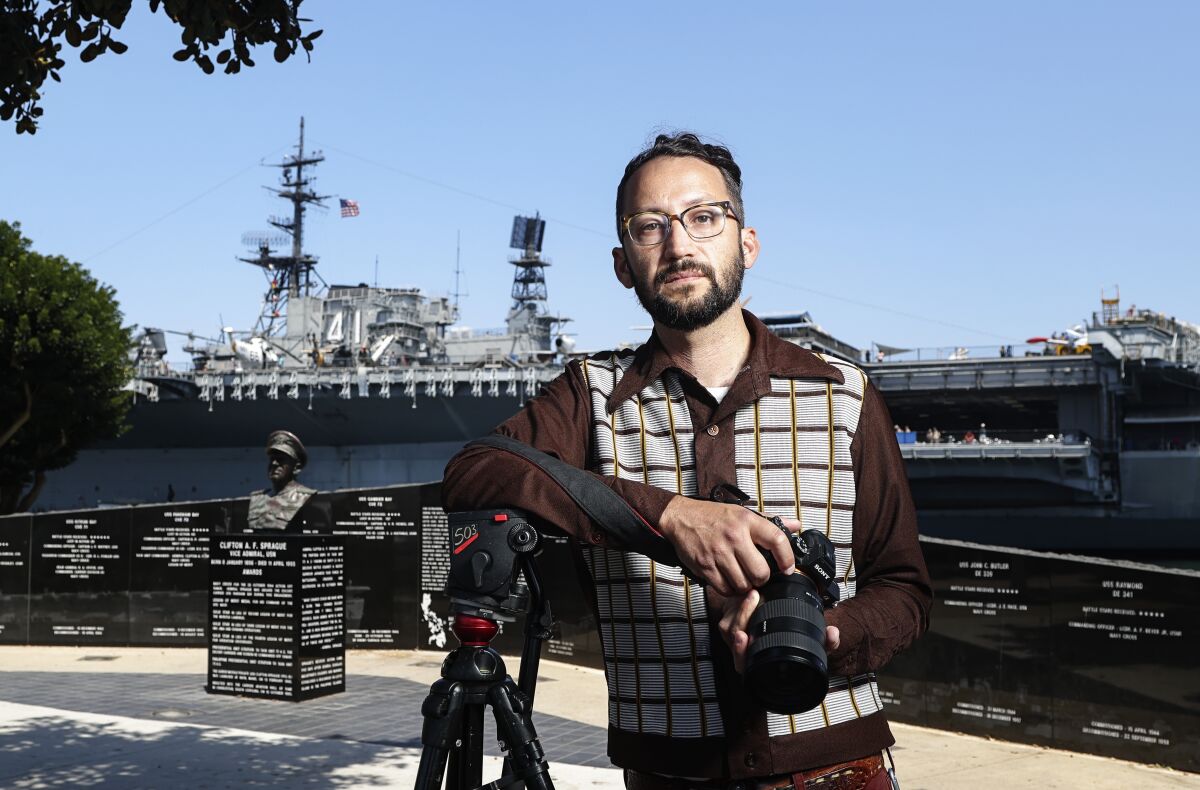 Filmmaker Evan Apodaca, holding a camera, is photographed near the Midway Museum.