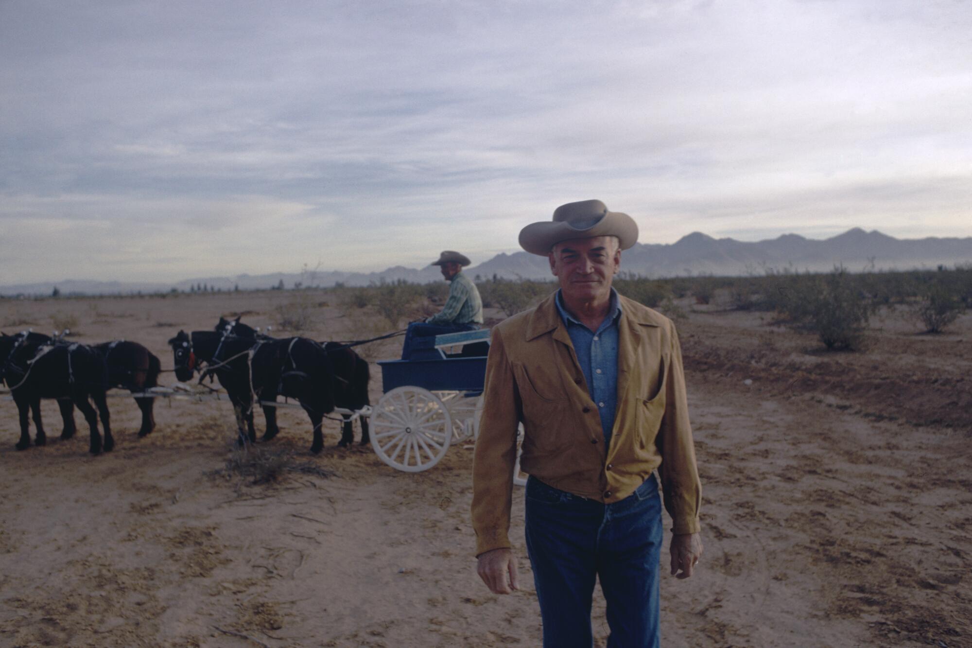 A middle-aged white man wearing a cowboy hat in front of a horse-drawn wagon