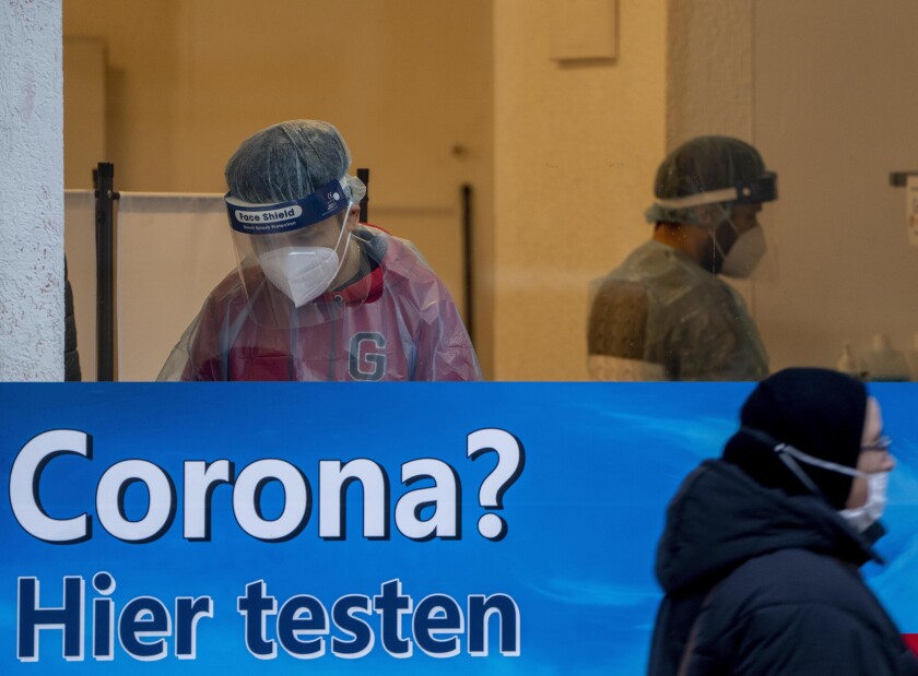 A woman walks past a Covid-19 test center in Frankfurt, Germany, Monday, Jan. 24, 2022, the day when German politicians discusses further measures to avoid the outspread of the coronavirus. Slogan read "Corona? test here". (AP Photo/Michael Probst)