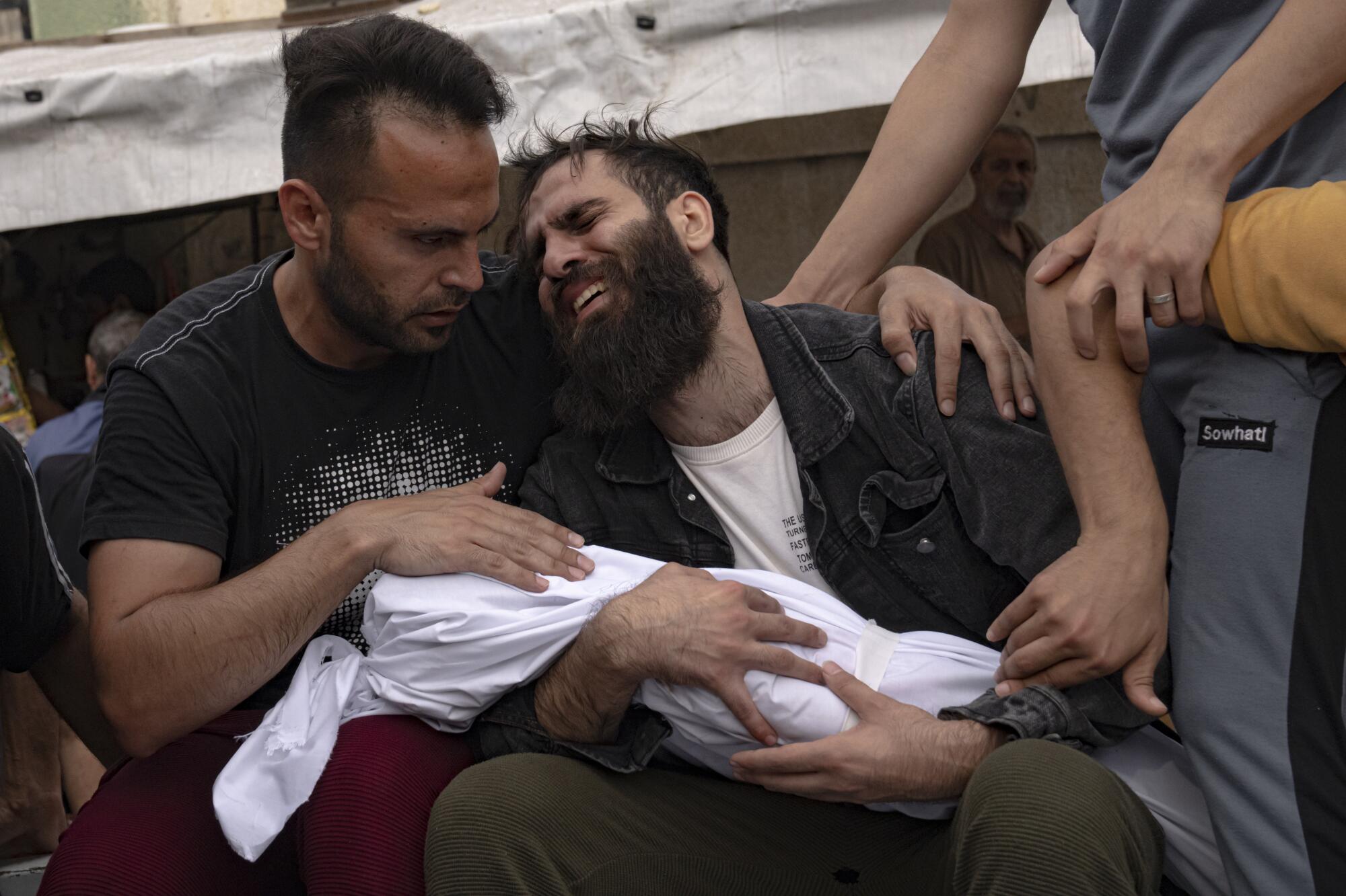 Two Palestinian men crying with the body of a small child wrapped in white cloth   
