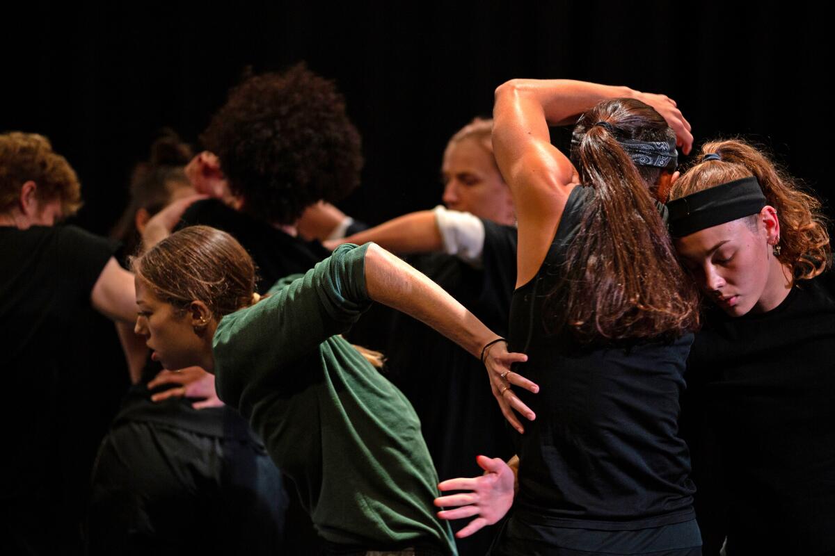 A group of dancers moving together with their hands reaching for one another. 