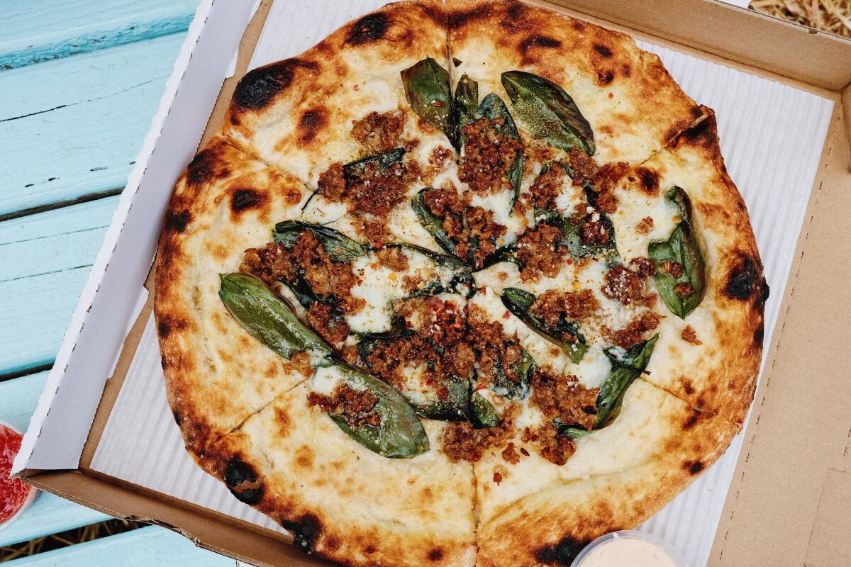 An overhead photo of a fava leaf and sausage pizza in a box at Fiorelli Pizza at The Cook's Garden in Venice.