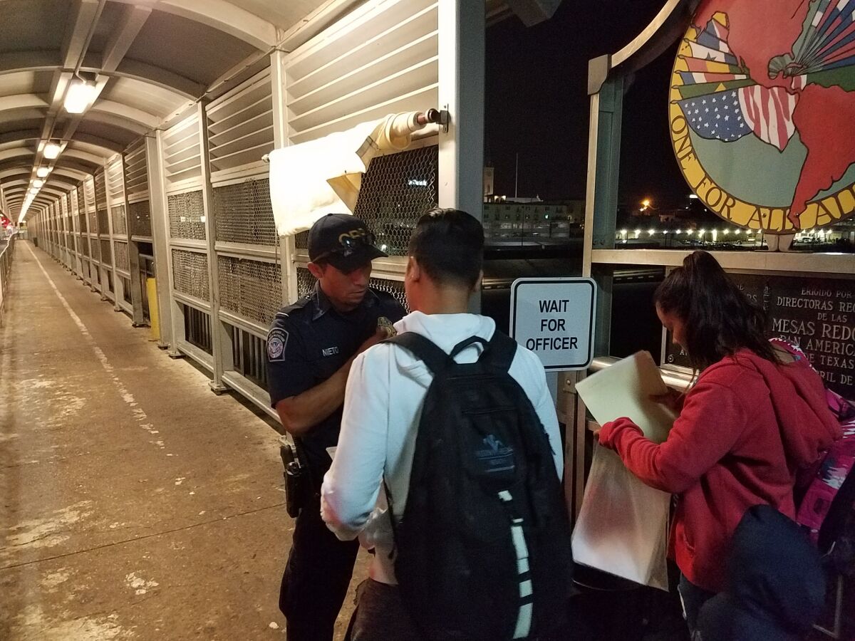 Salvadoran asylum seeker Katherinne Fuentes, 20, right, prepares to show a U.S. Customs officer her court paperwork so she can enter Laredo to attend her hearing at the new tent court.