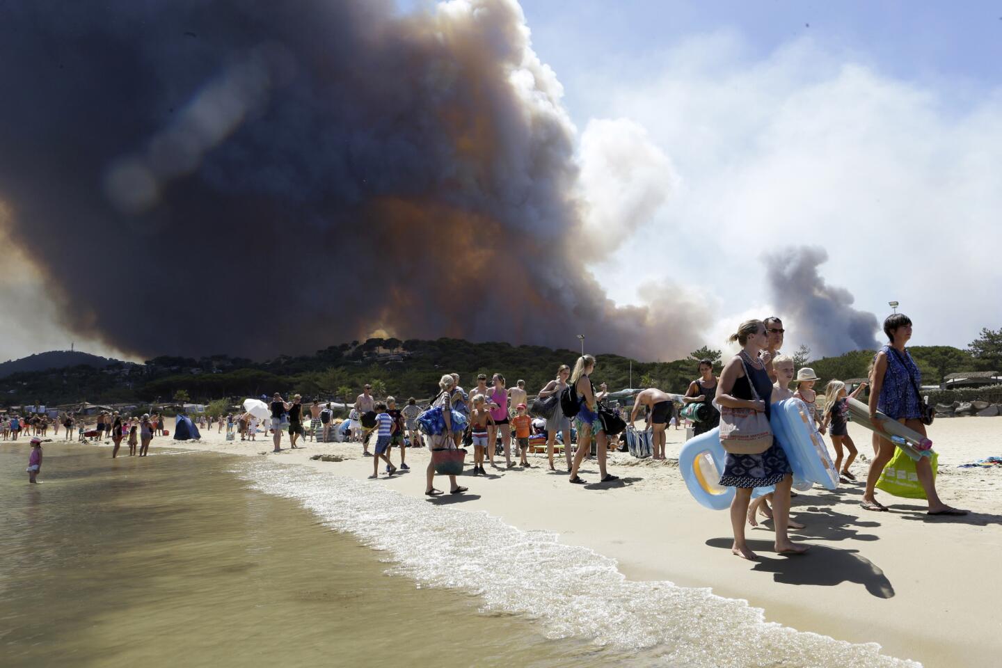 Sunbathers are evacuated from the beach in Le Lavandou, in the French Riviera, as plumes of smoke rise from a nearby wildfire on July 26, 2017. French authorities ordered the evacuation of up to 12,000 people around a picturesque hilltop town in the southern Cote d'Azur region as fires hopscotched around the Mediterranean coast for a third day.