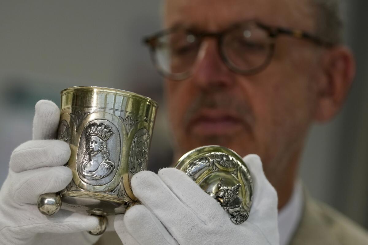 A museum curator wearing gloves holds a silver object. 
