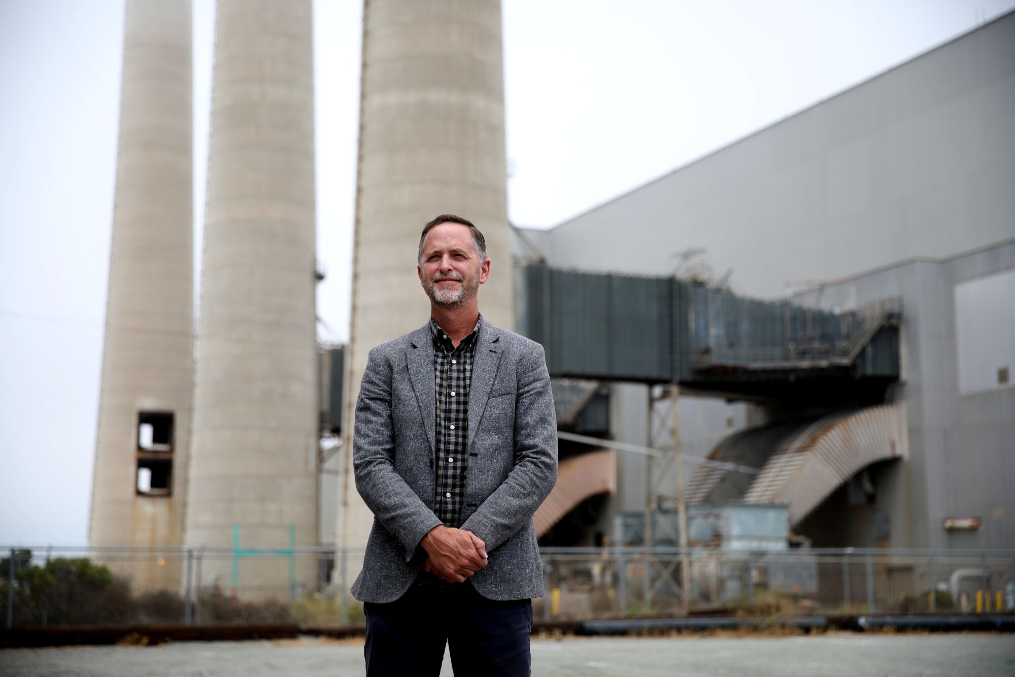 A man stands in front of a power plant's three smokestacks