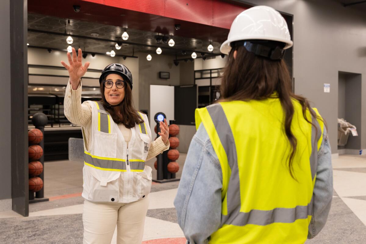 Two women in safety vests and hard hats inside a stadium