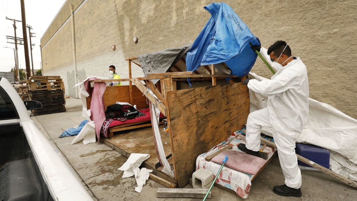 Jesus Sanchez, left, and Javier Villarreal with the Los Angeles Bureau of Sanitation secure the scene as crews arrive to clean up a homeless encampment.