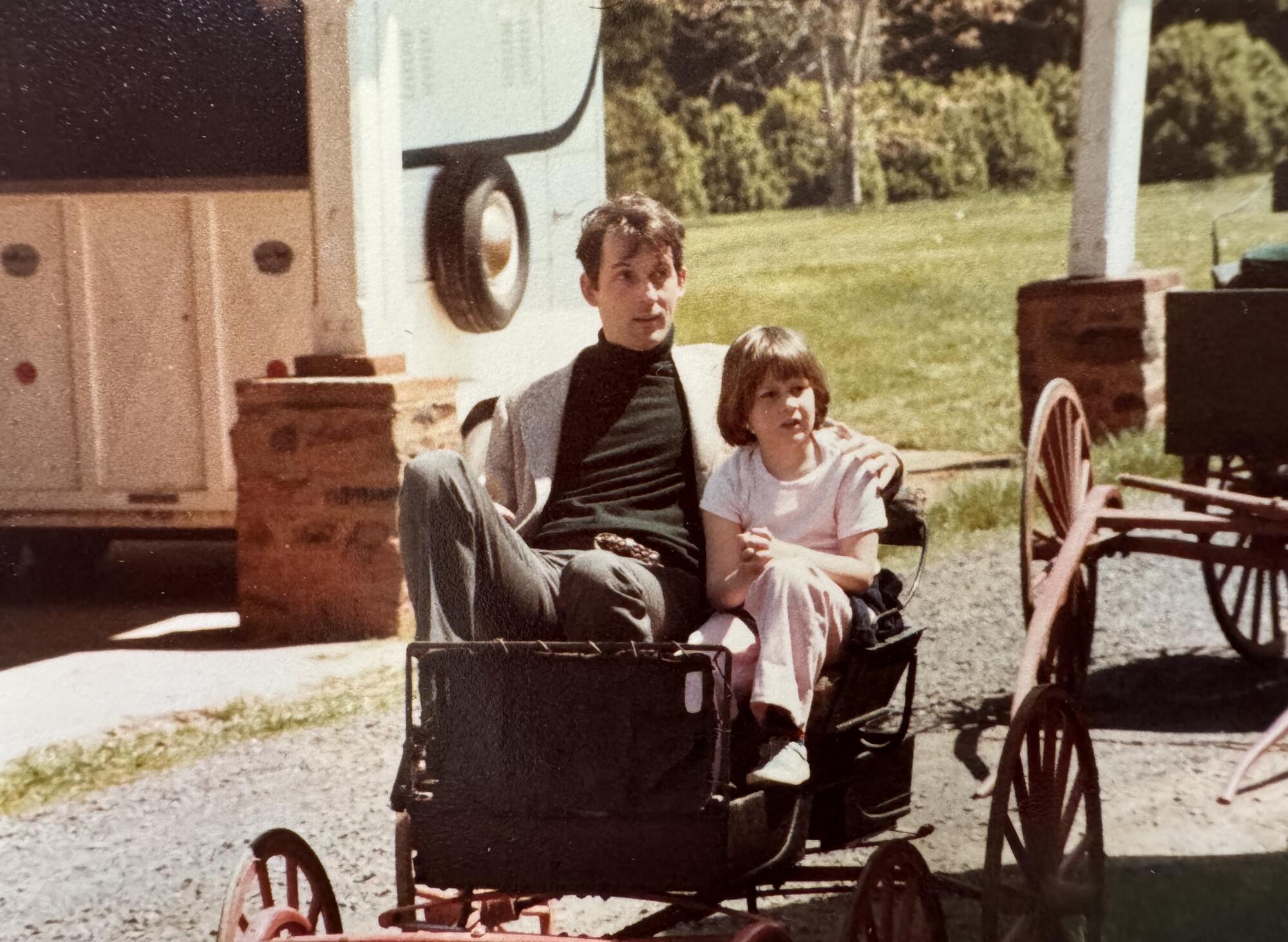 A father and daughter sit together in a cart.  