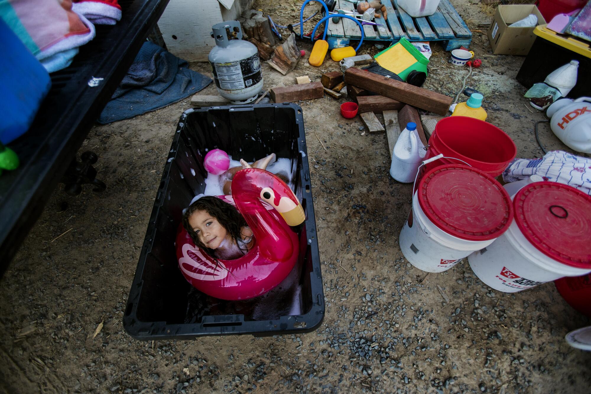 A little girl plays with an inflatable flamingo inside a bin filled with water.
