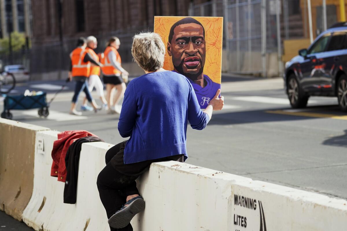 A woman holds a George Floyd picture while seated on a concrete barrier