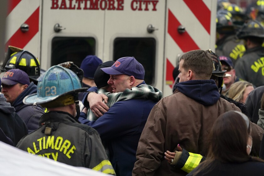 People embrace one another after a deceased firefighter was put into an ambulance after being pulled out of a collapsed building while battling a two-alarm fire at a vacant row home, Monday, Jan. 24, 2022, in Baltimore. Officials said several firefighters died during the blaze. (AP Photo/Julio Cortez)