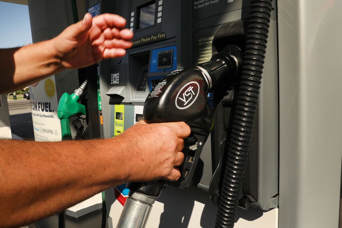 A hand holds a gas pump while another hand reaches toward the pump's display.