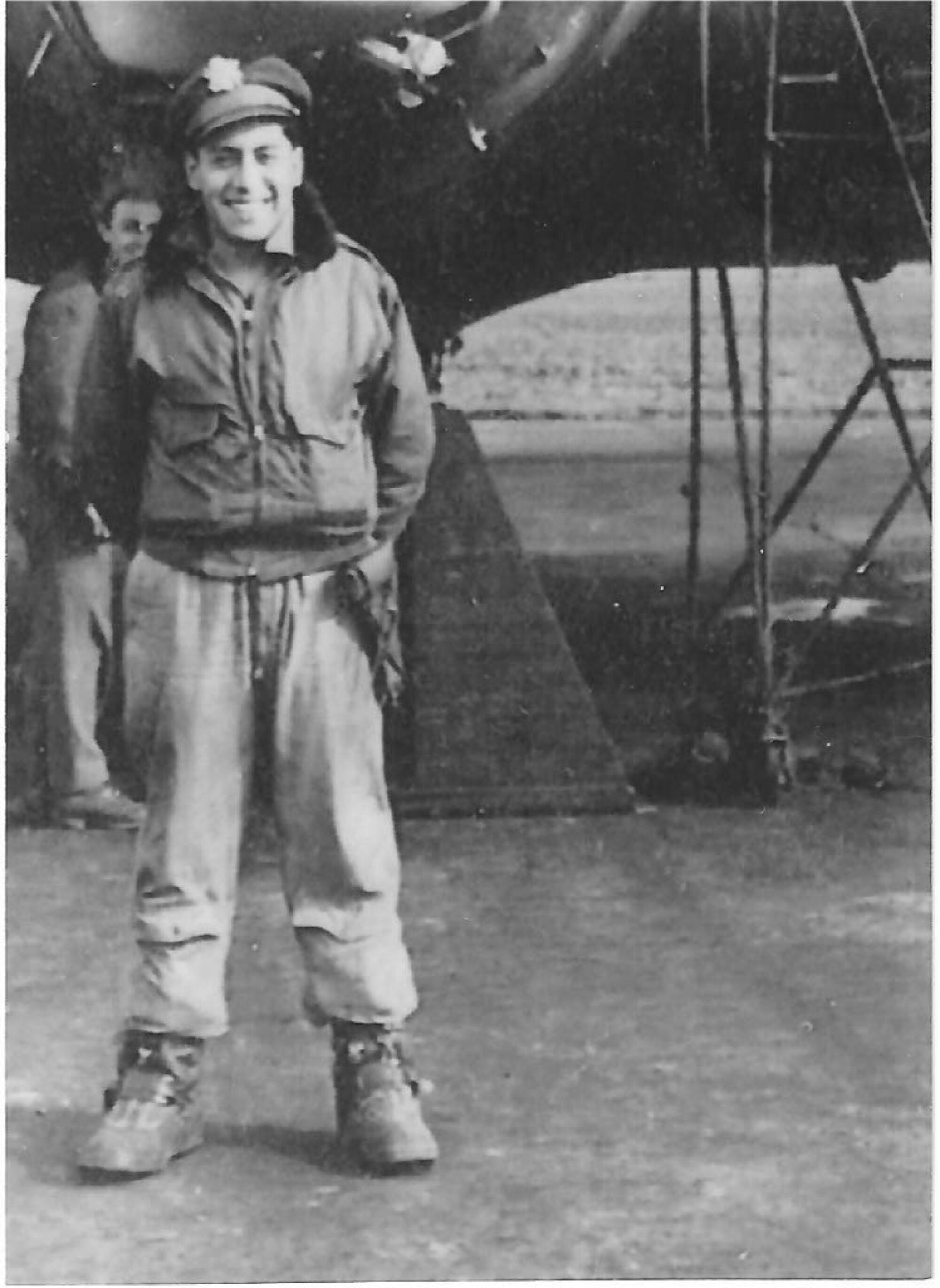 A smiling man in a military pilot's cap and uniform stands near a plane 
