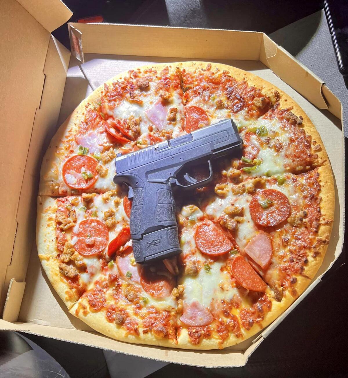 A handgun is on a pizza in an open box.
