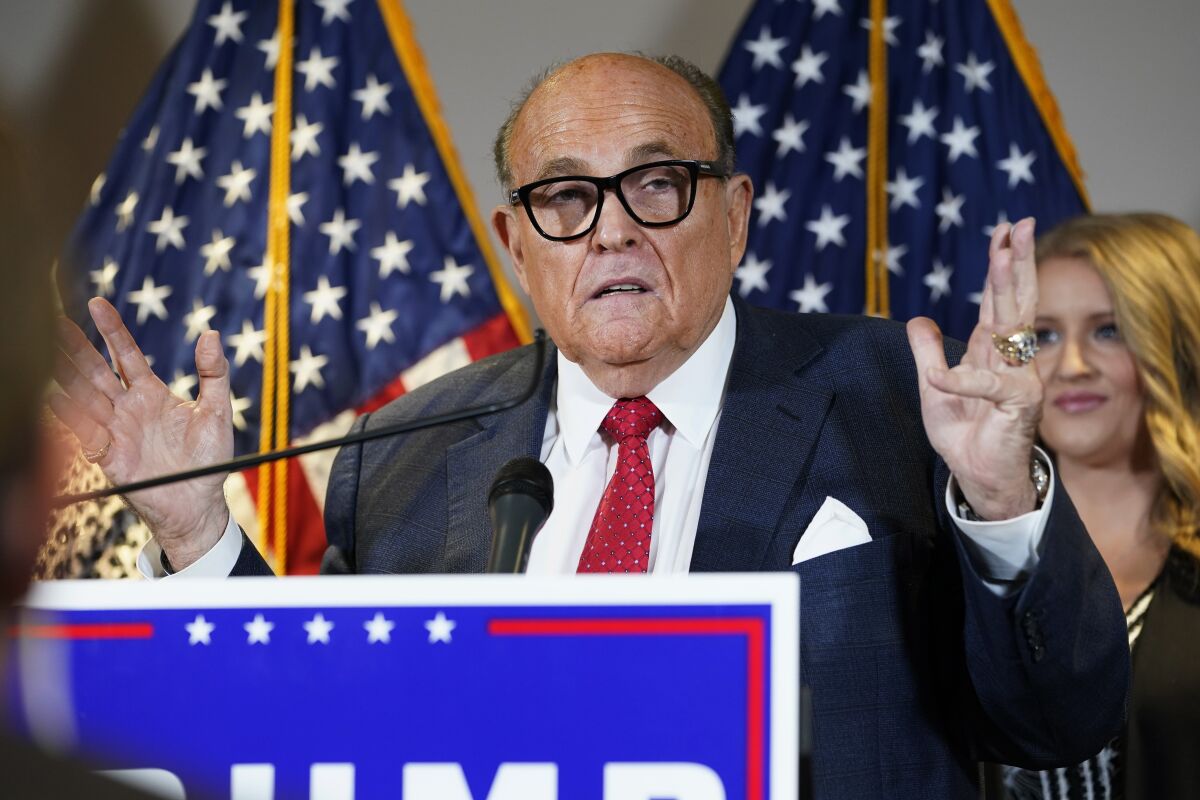 Rudolph W. Giuliani speaks at a lectern while a woman stands behind him.