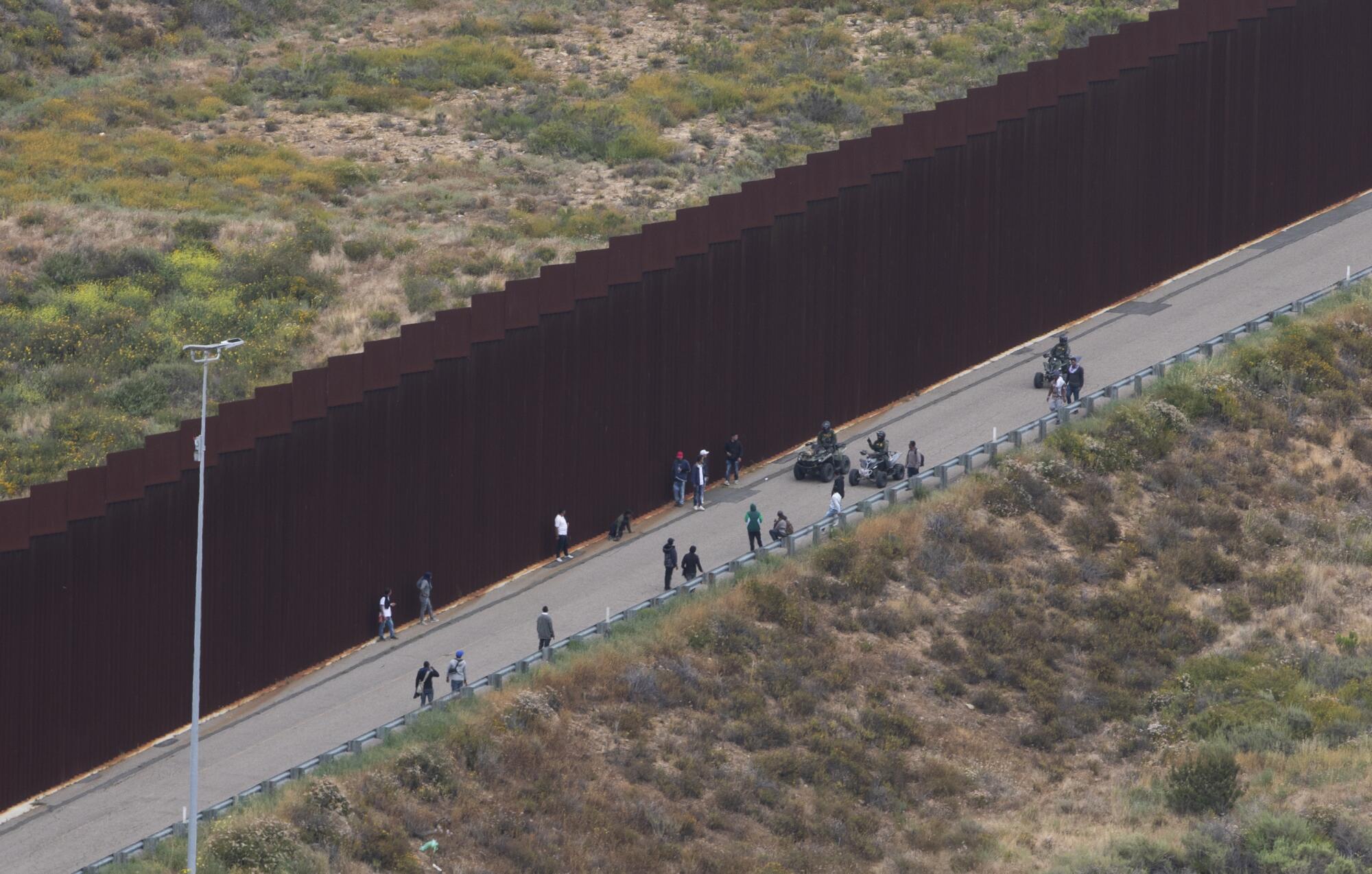 Border Patrol agents push a group of male migrants back between the border walls.