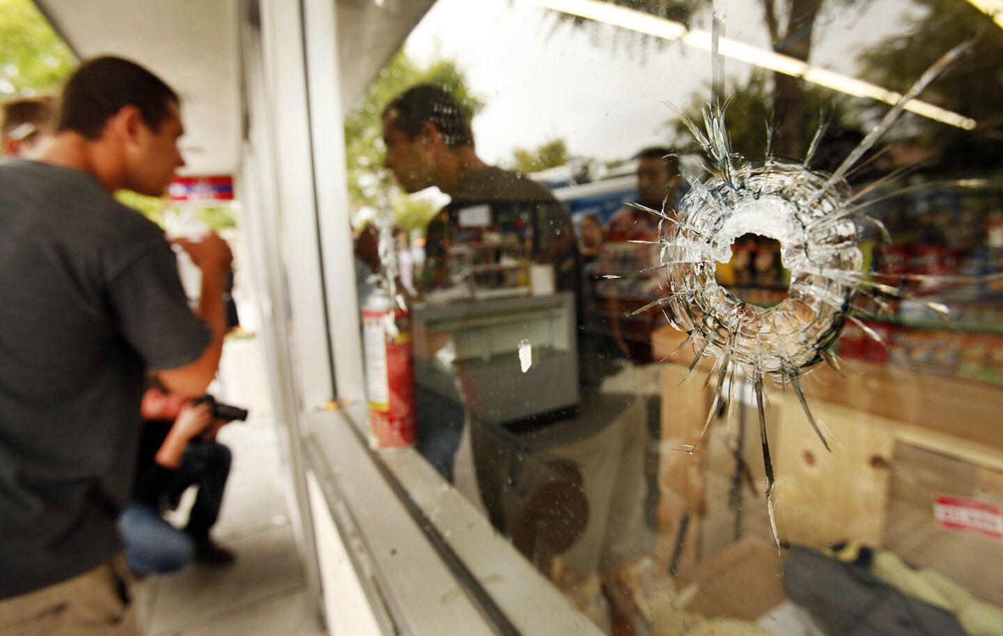 People look through a window pocked with bullet holes at the IV Deli Mart in Isla Vista, near UC Santa Barbara.