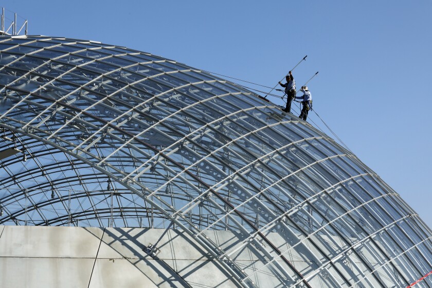 Window washers Mario Guzman, left, and Jesus Garcia, right, clean the dome of the Academy Museum of Motion Pictures.