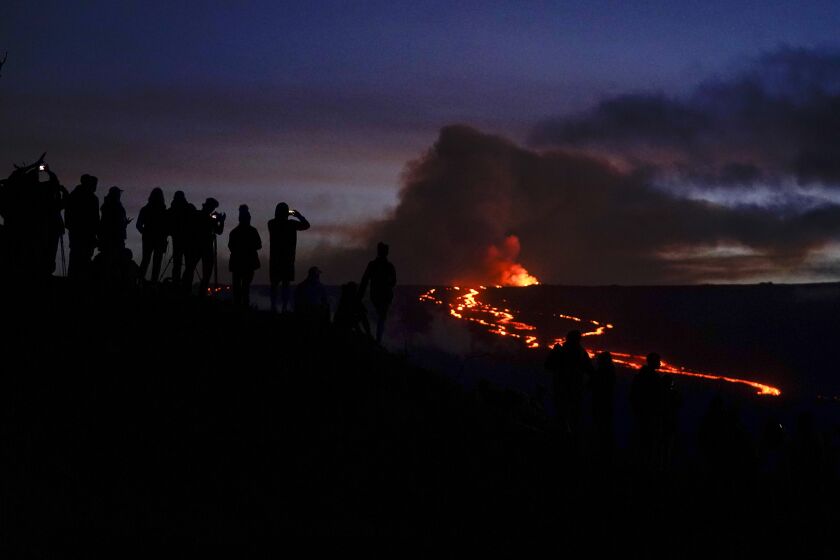 People watch and record images of lava from the Mauna Loa volcano Thursday, Dec. 1, 2022, near Hilo, Hawaii. (AP Photo/Gregory Bull)