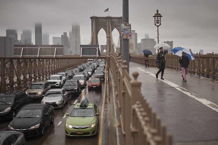 Personas con sombrillas caminan a un costado de los vehículos por el Puente de Brooklyn, luego de las fuertes lluvias del viernes 29 de septiembre de 2023, en Nueva York. (AP Foto/Andres Kudacki)