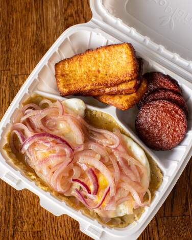 A foam container of mangu los tres golpes (mashed, boiled plantains, fried eggs, pickled red onion, fried salami and cheese) 