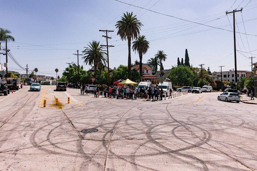 Looping black tire marks fill an intersection with a crowd of people gathered nearby