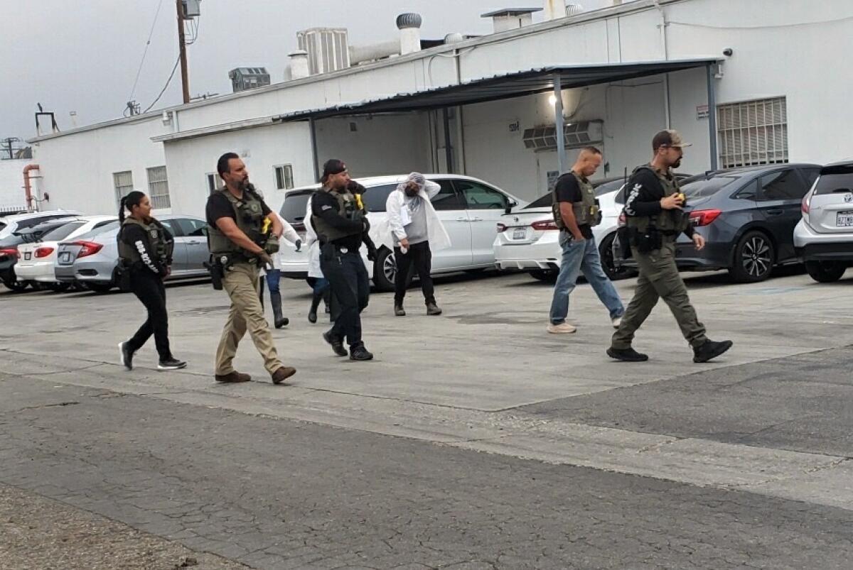 People, some in law enforcement uniforms, walk through a parking lot in an industrial area.