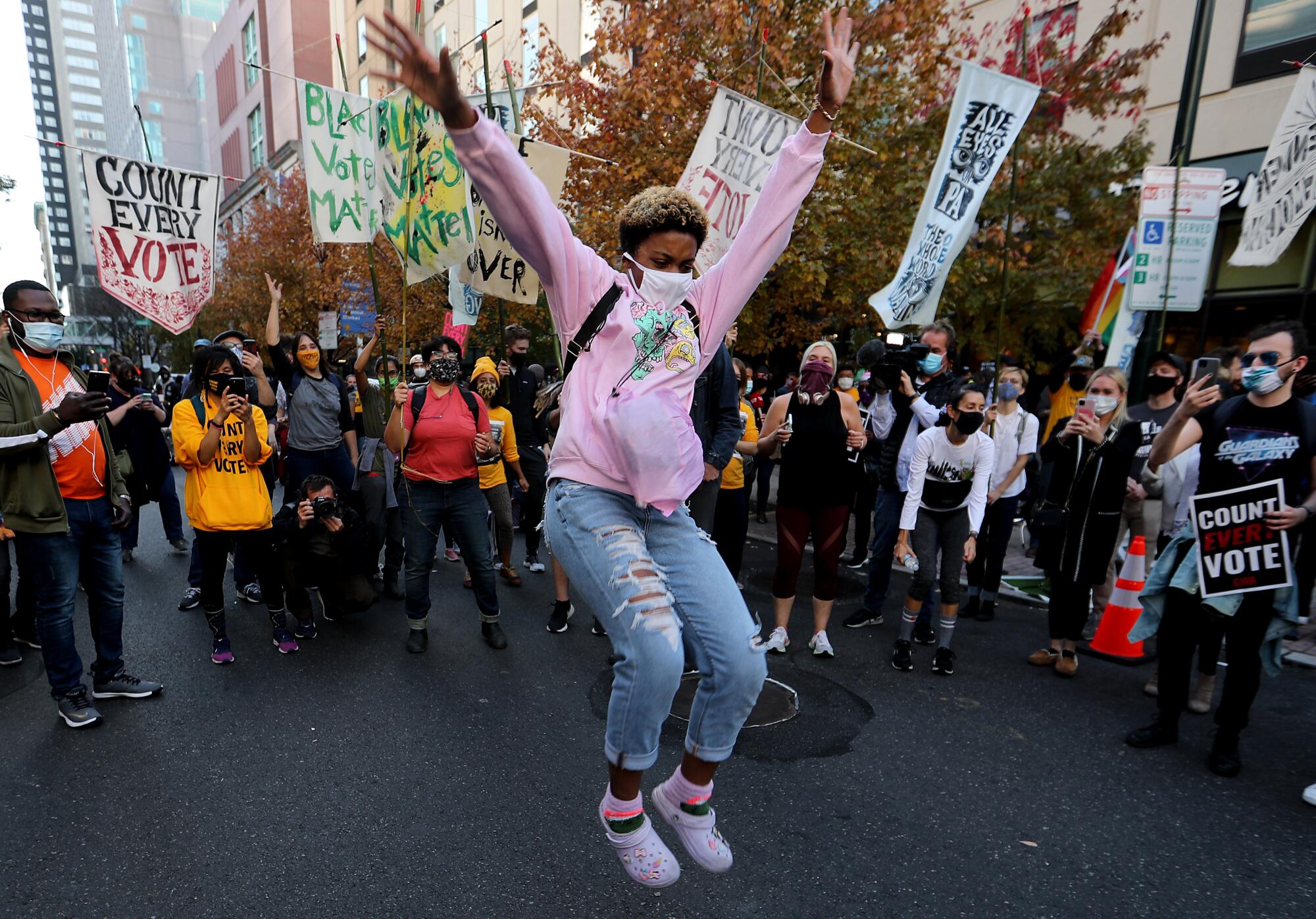 A woman in a mask jumps with her hands in the air in the middle of a circle of dancing protesters