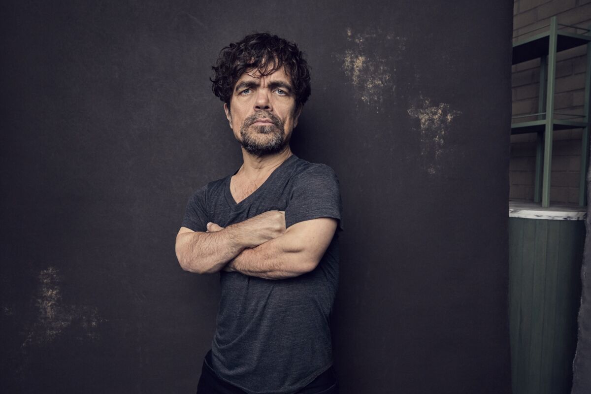 Actor Peter Dinklage stands with his arms crossed in front of his chest.