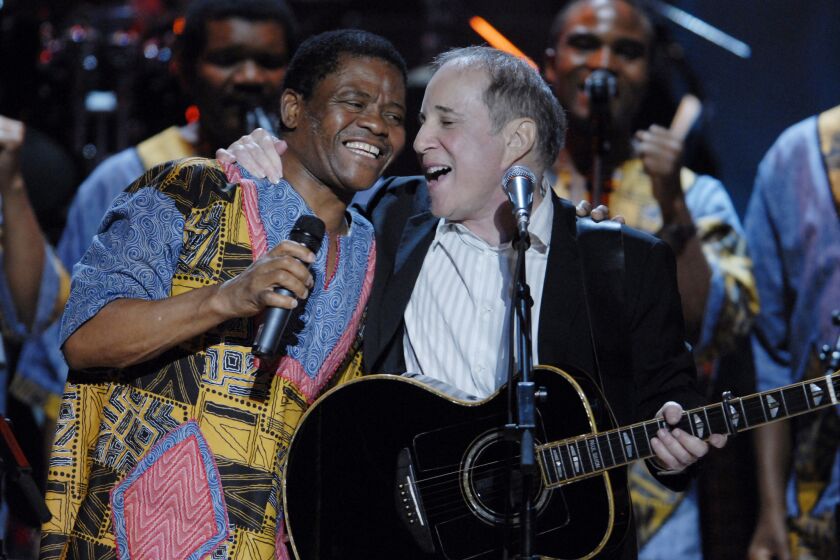 Paul Simon, shown in performance with South African singer Joseph Shabalala and his Ladysmith Black Mambazo vocal group, is the subject of a forthcoming biography to be written by former Times pop music critic Robert Hilburn.