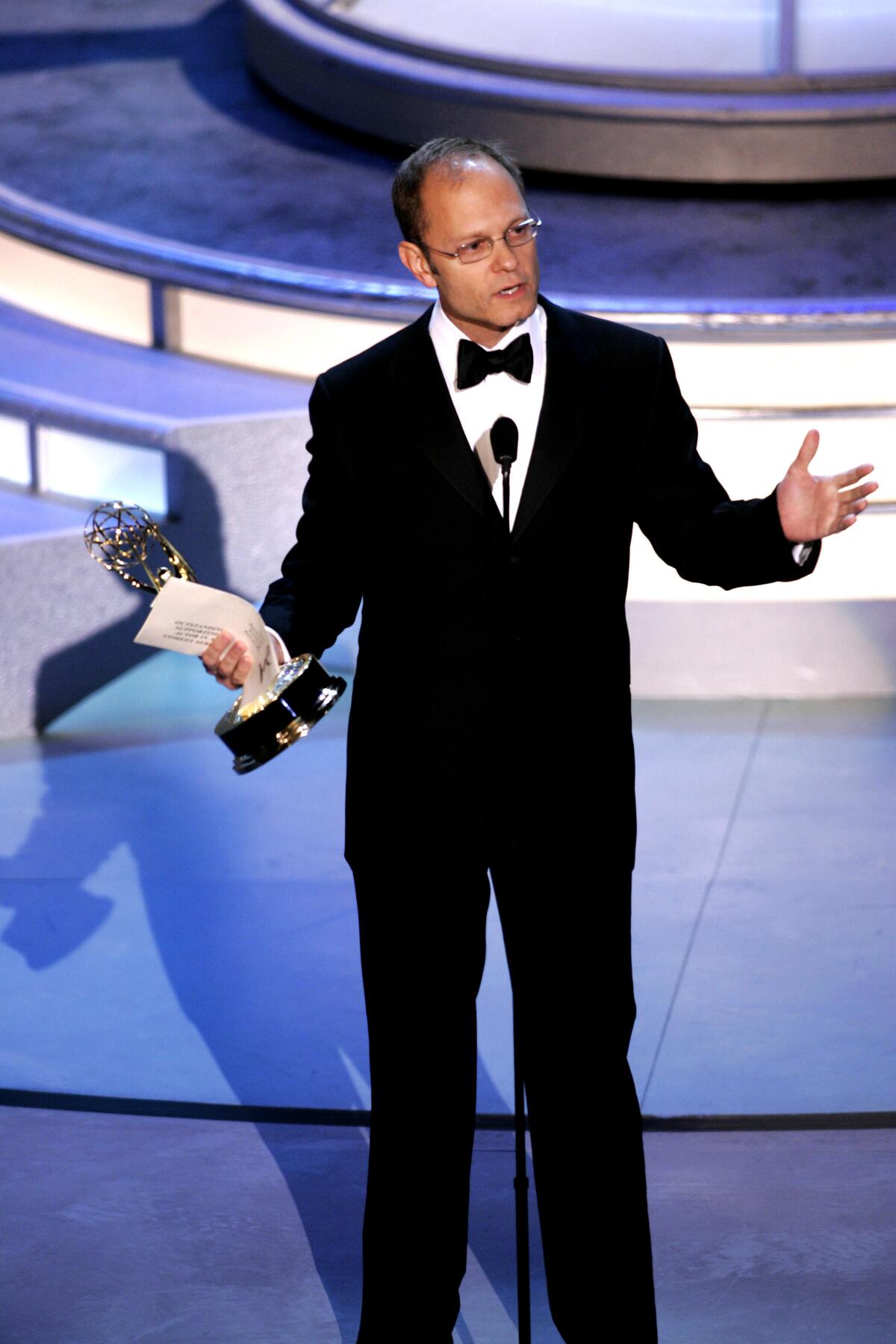 David Hyde Pierce wears a tuxedo and gestures while holding his Emmy onstage at the 2004 ceremony.
